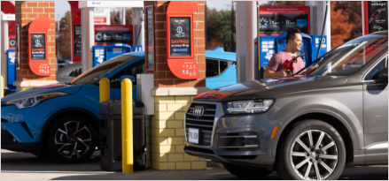 Person filling up their silver car s gas tank at red gas pump