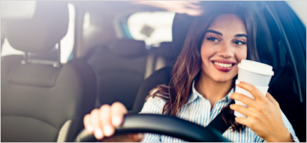 Woman with her cup of coffee smiling driving her car